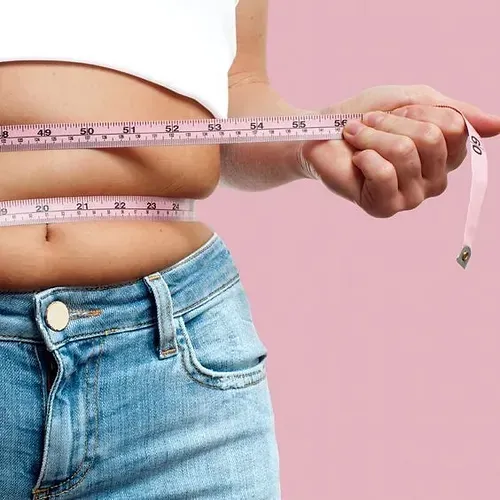 A woman is measuring her waist with a tape measure