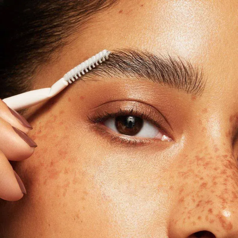A woman is brushing her eyebrows with a brush