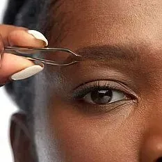 A woman is using tweezers to trim her eyebrows