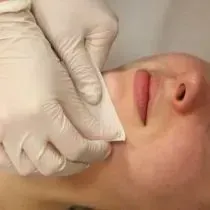 A person wearing gloves is cleaning a woman 's face with a cloth