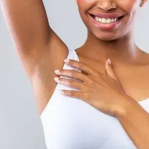 A woman in a white tank top is smiling and holding her arm up