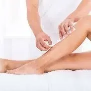 A woman is getting her legs waxed by a man