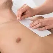 A woman is waxing a man 's chest with wax strips