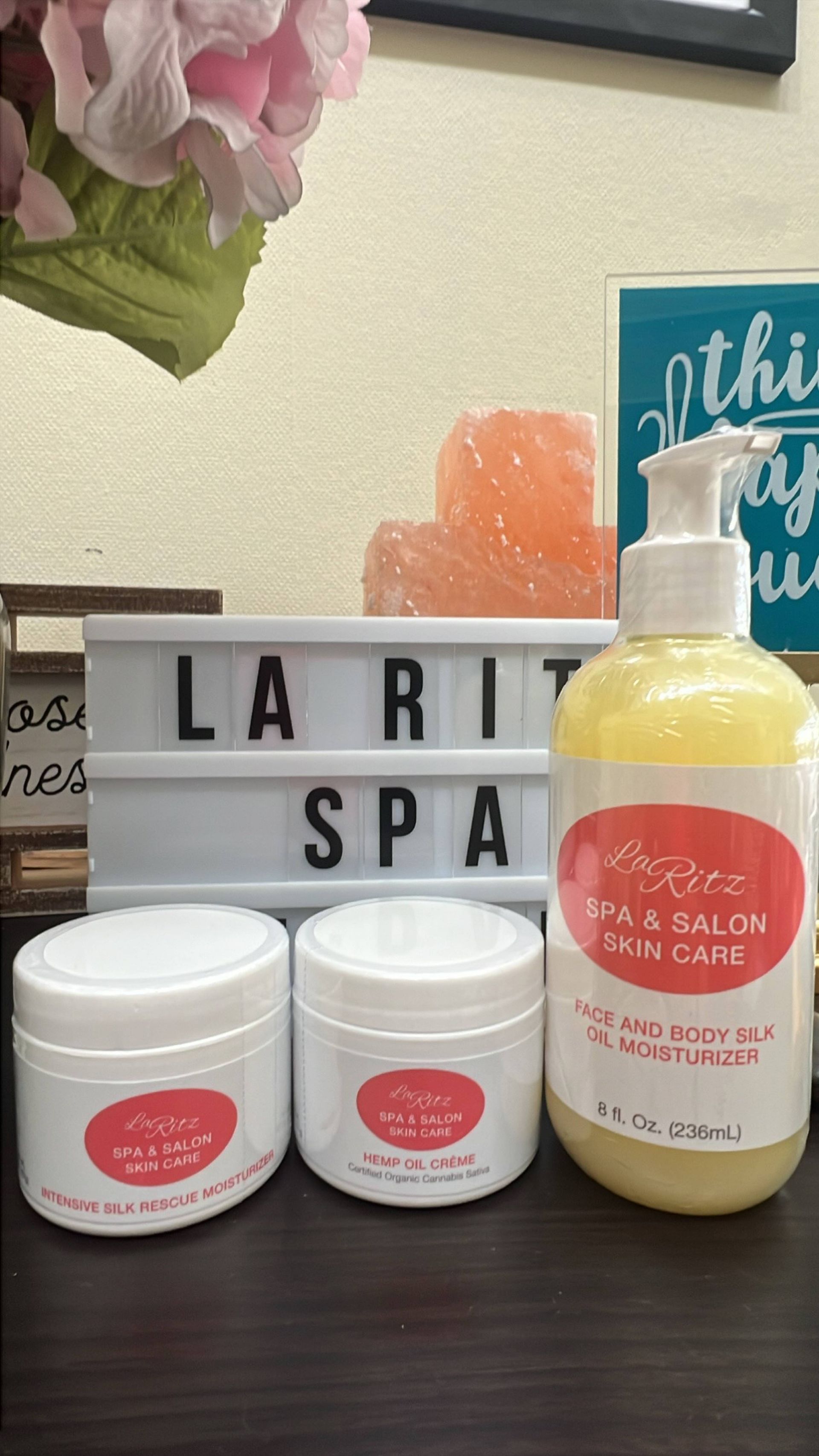 A bottle of lotion and three jars of cream are on a table next to a sign that says la rit spa.