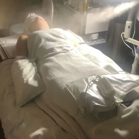 A person is laying on a bed wrapped in a white blanket.