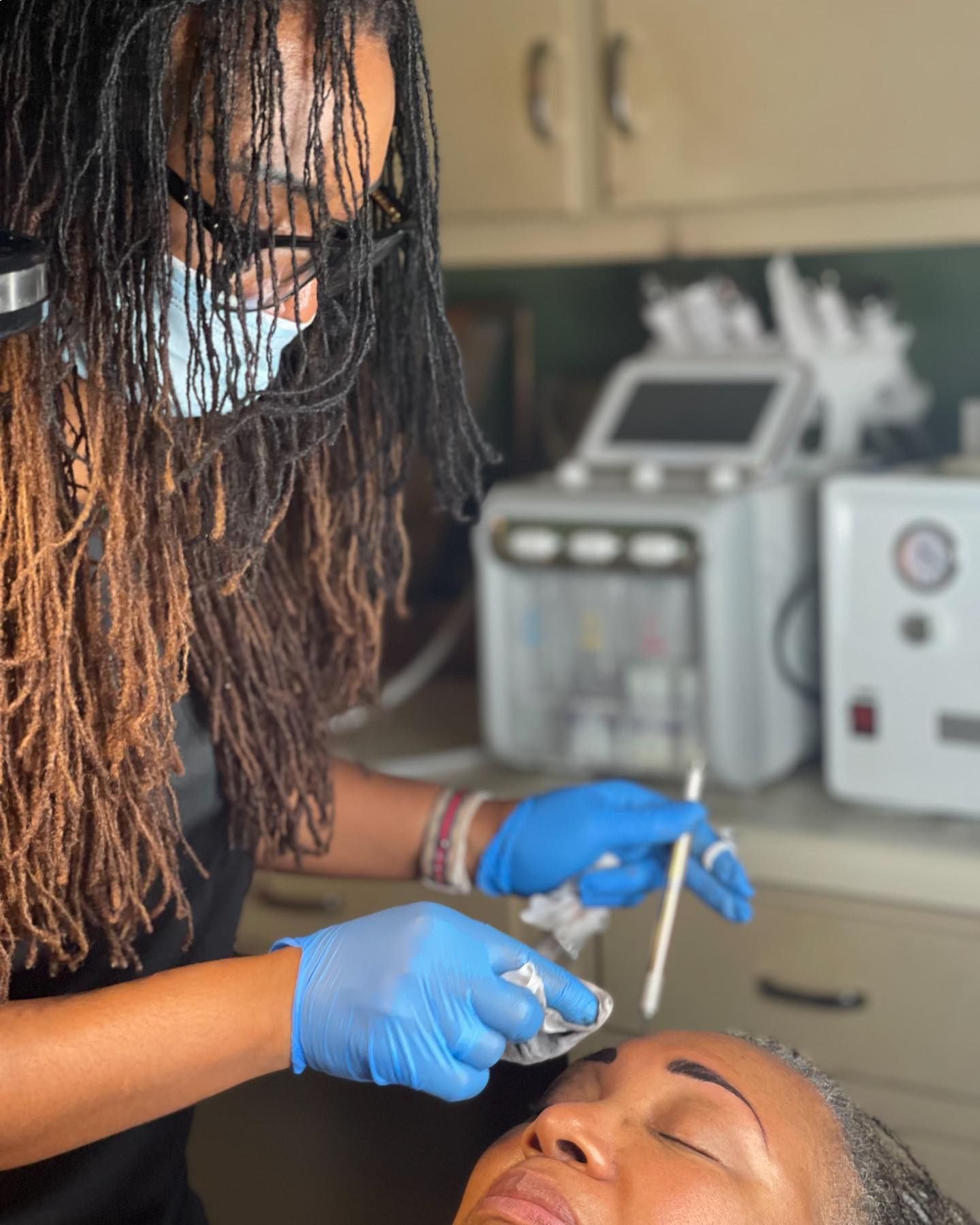 A woman wearing a mask and blue gloves is cleaning a woman 's face.