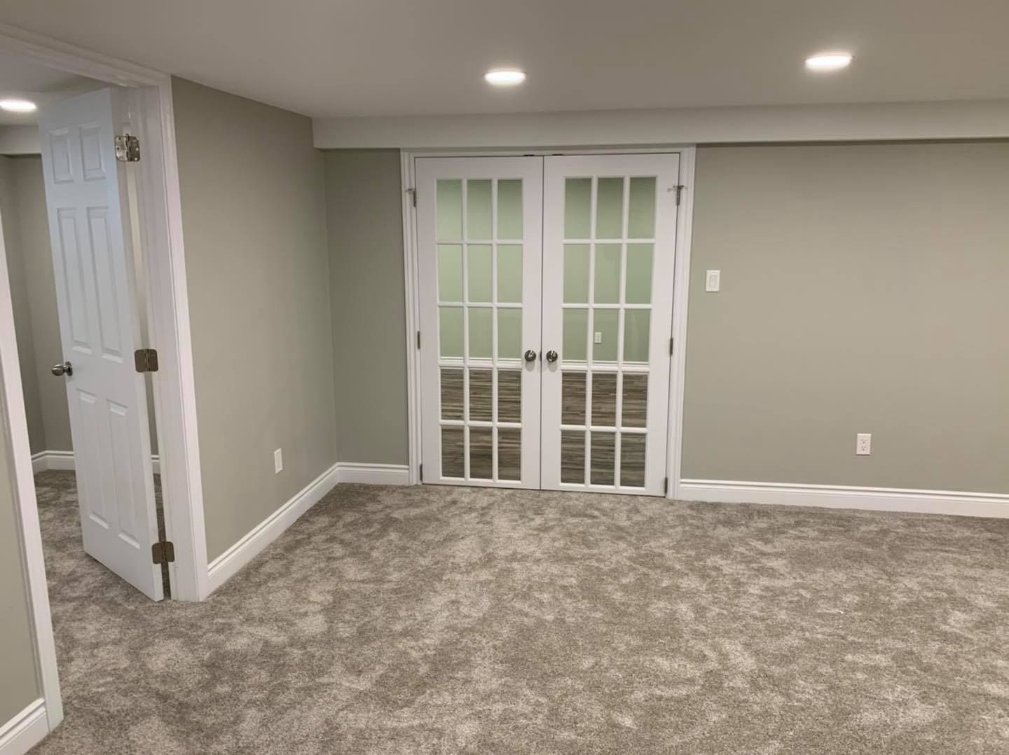 An empty basement with a carpeted floor and french doors.