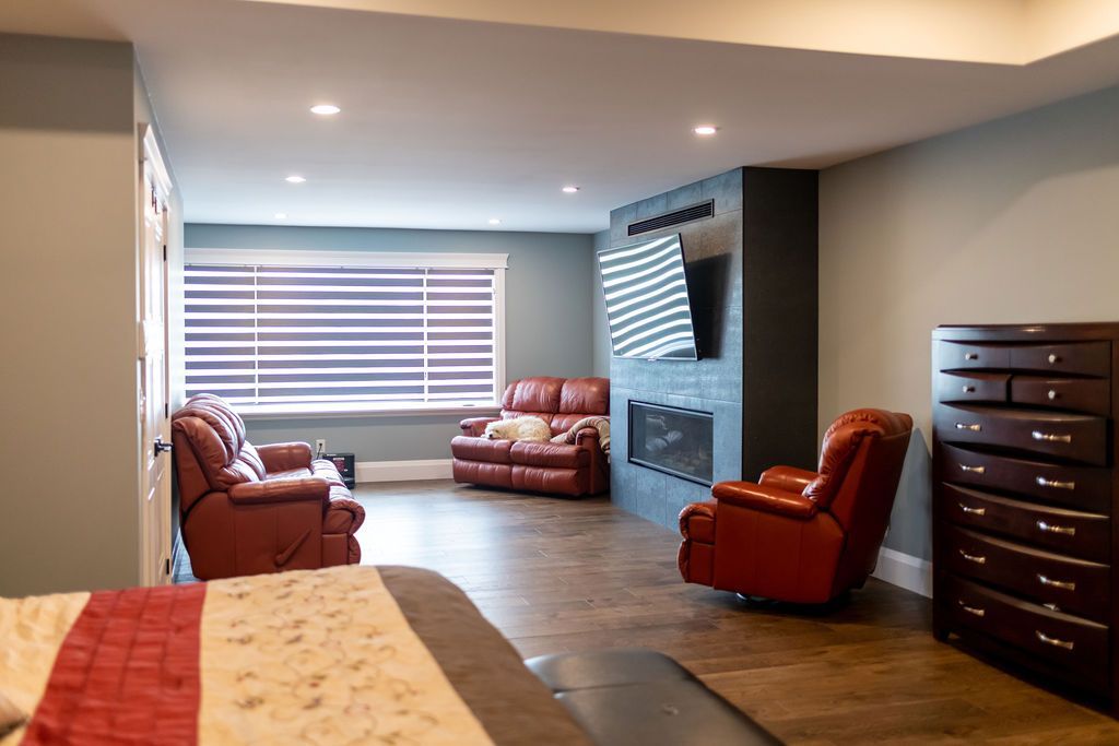 A bedroom with a bed , dresser , chairs and a fireplace.