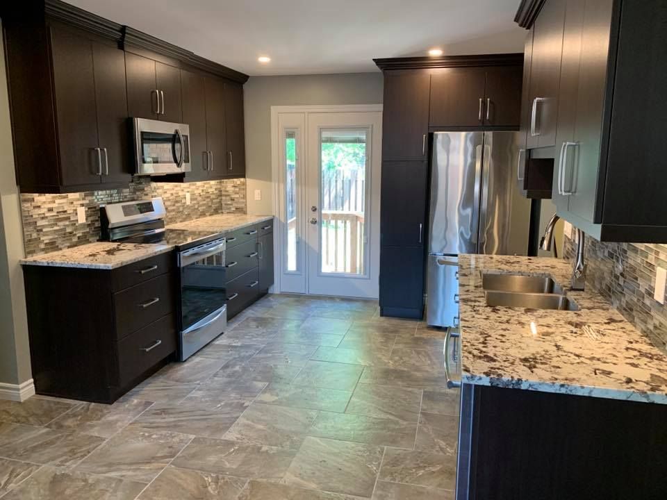 Dark kitchen with granite counters, stainless steel appliances, and a door to the outdoors.
