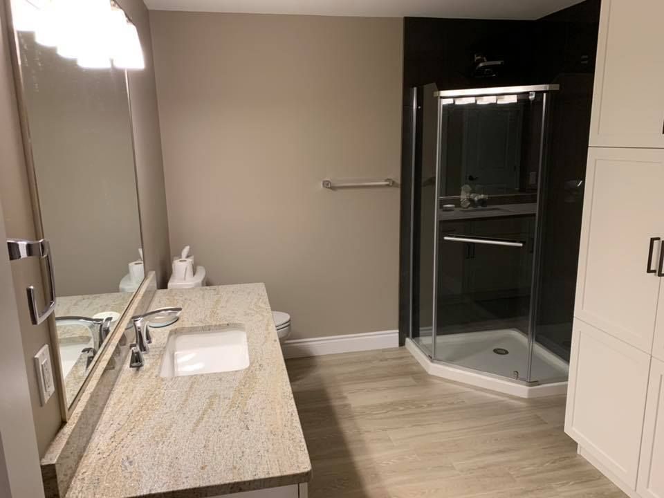 Bathroom with beige walls, granite countertop, glass shower, and white cabinets.