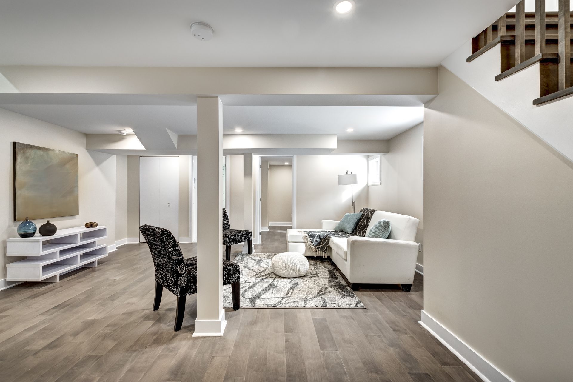 A living room in a basement with a couch , chairs , and stairs.