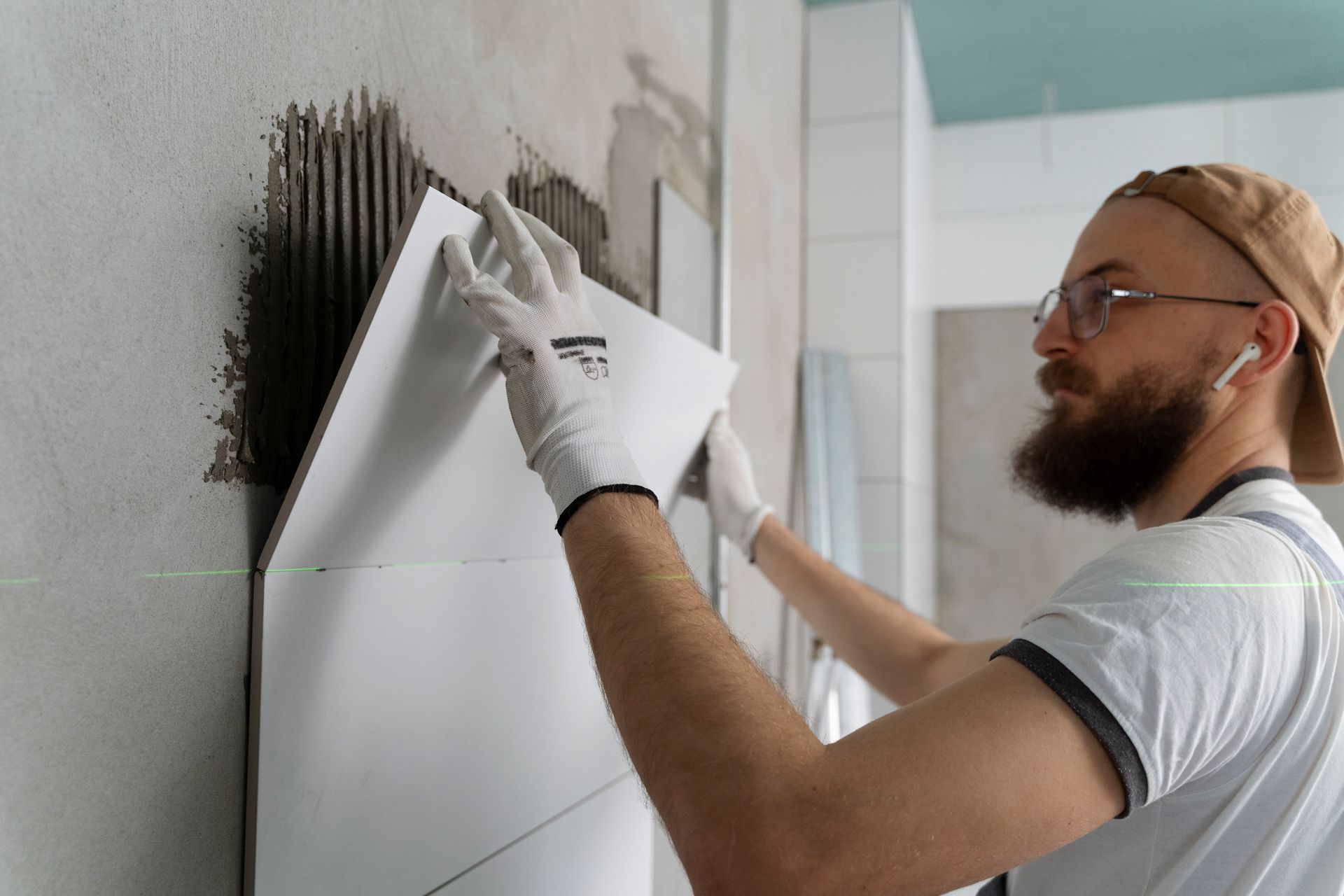 A man with a beard is applying tile to a wall.