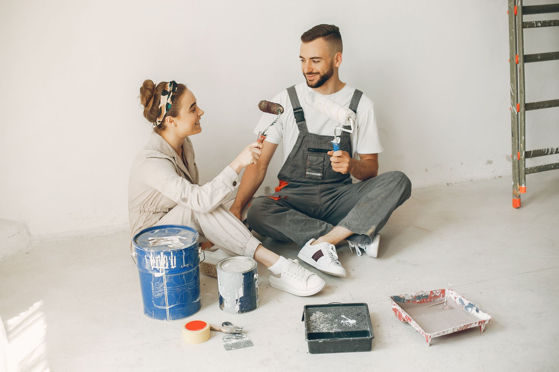 A man and a woman are sitting on the floor painting a wall.