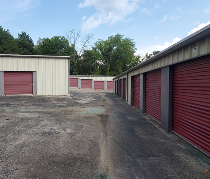 Storage units with red doors, off-white walls, and asphalt ground under a blue sky.