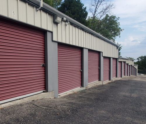 Red storage unit doors in a row, on a blacktop surface. Beige building with gray trim.