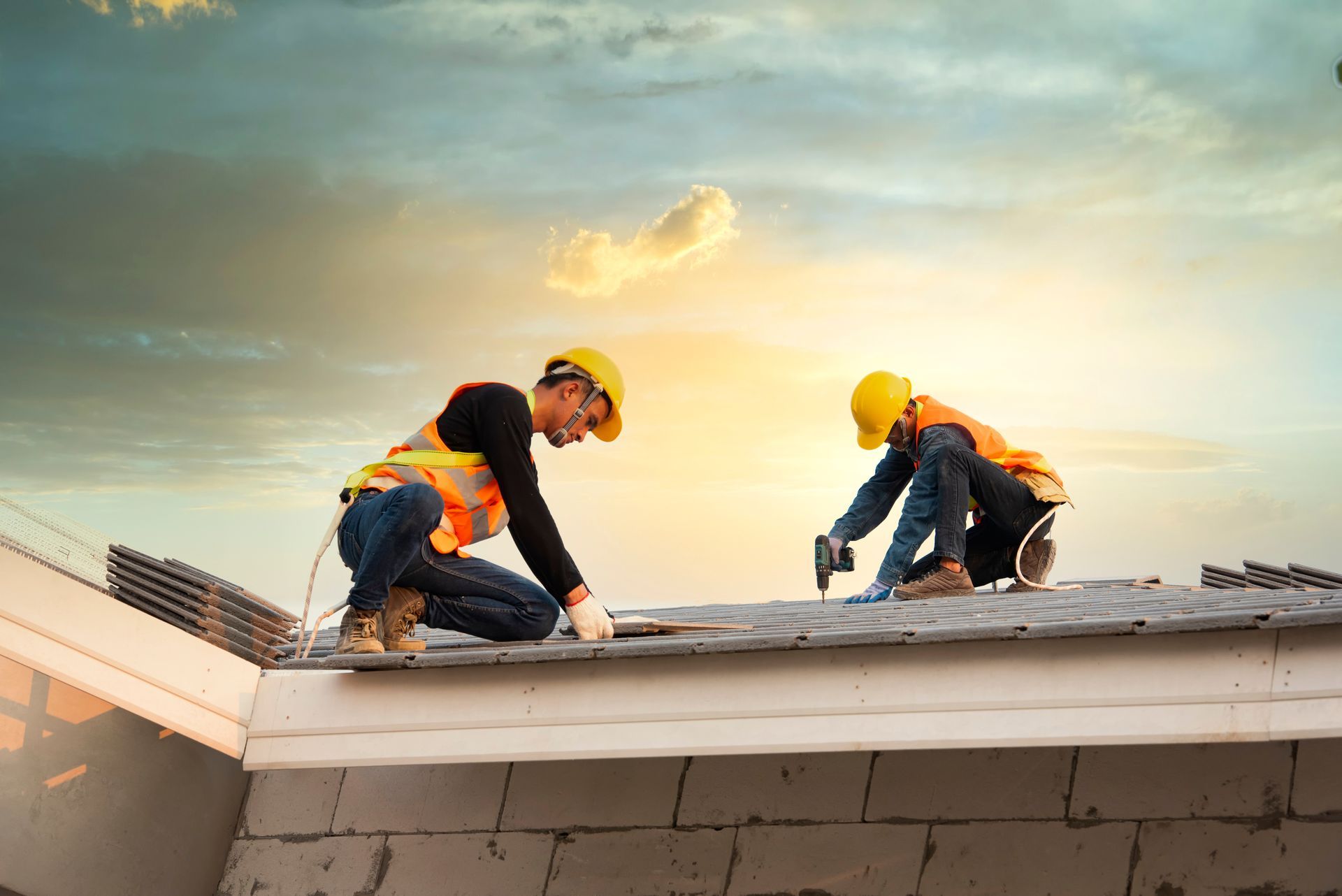 Workers install roofing panels on house roof at sunset.