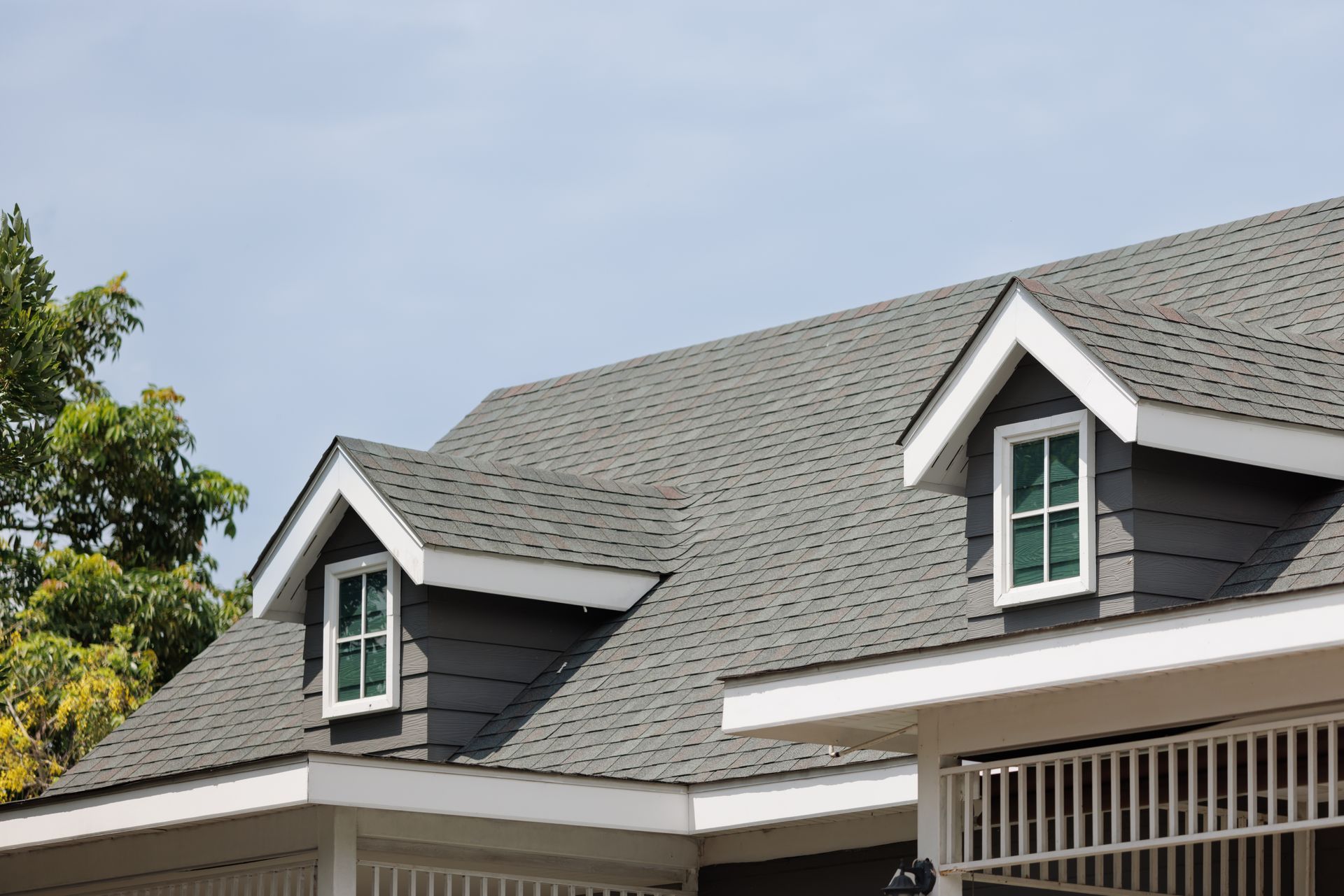 Gray shingle roof with dormer windows and white trim on suburban house.
