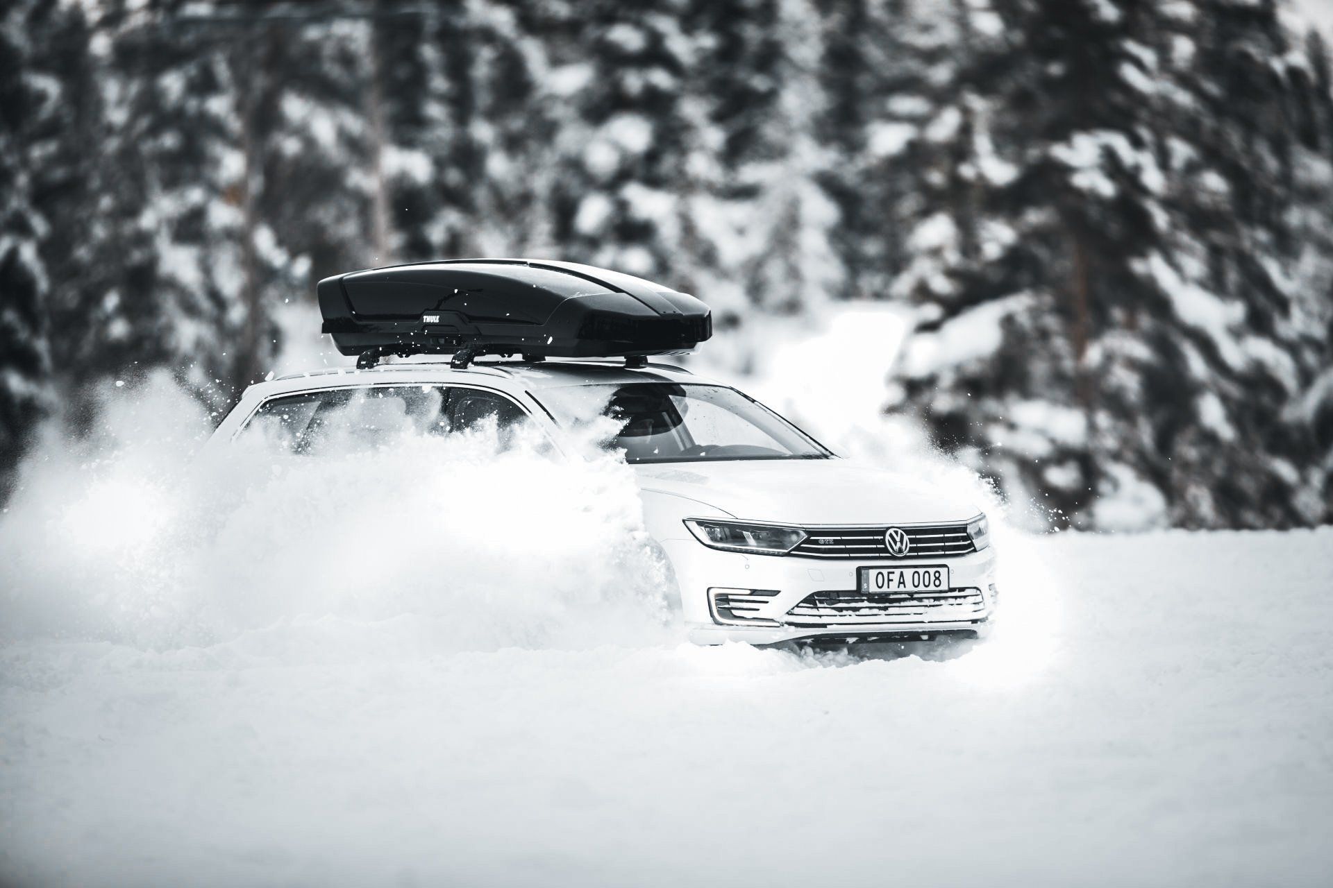 Een auto met daarop een dakkoffer rijdt door de sneeuw.