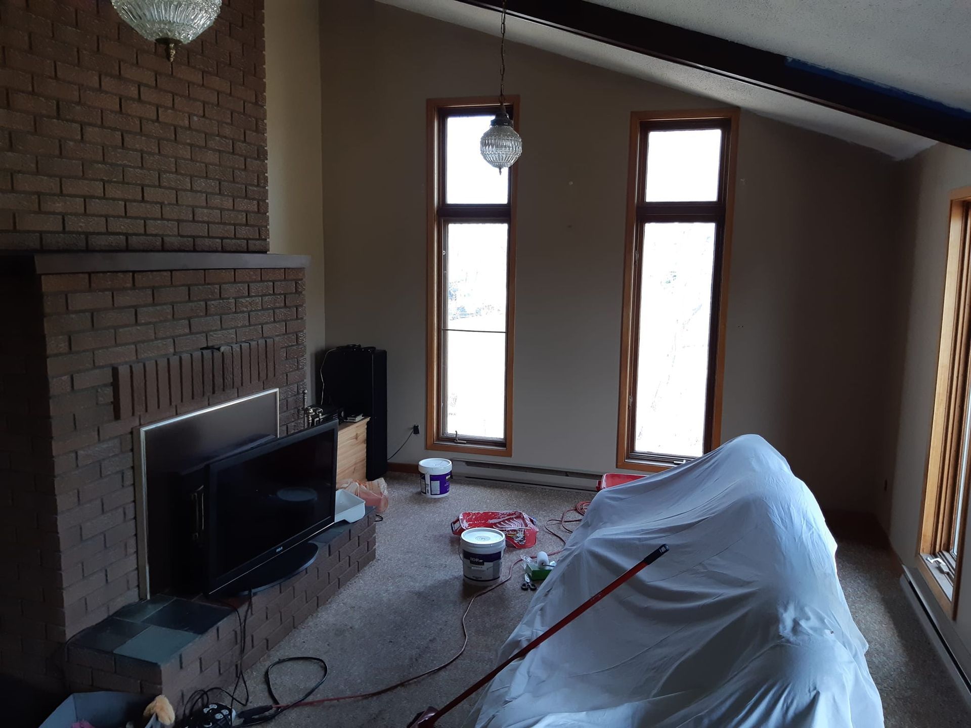 Living room with a brick fireplace and large windows, currently under renovation.