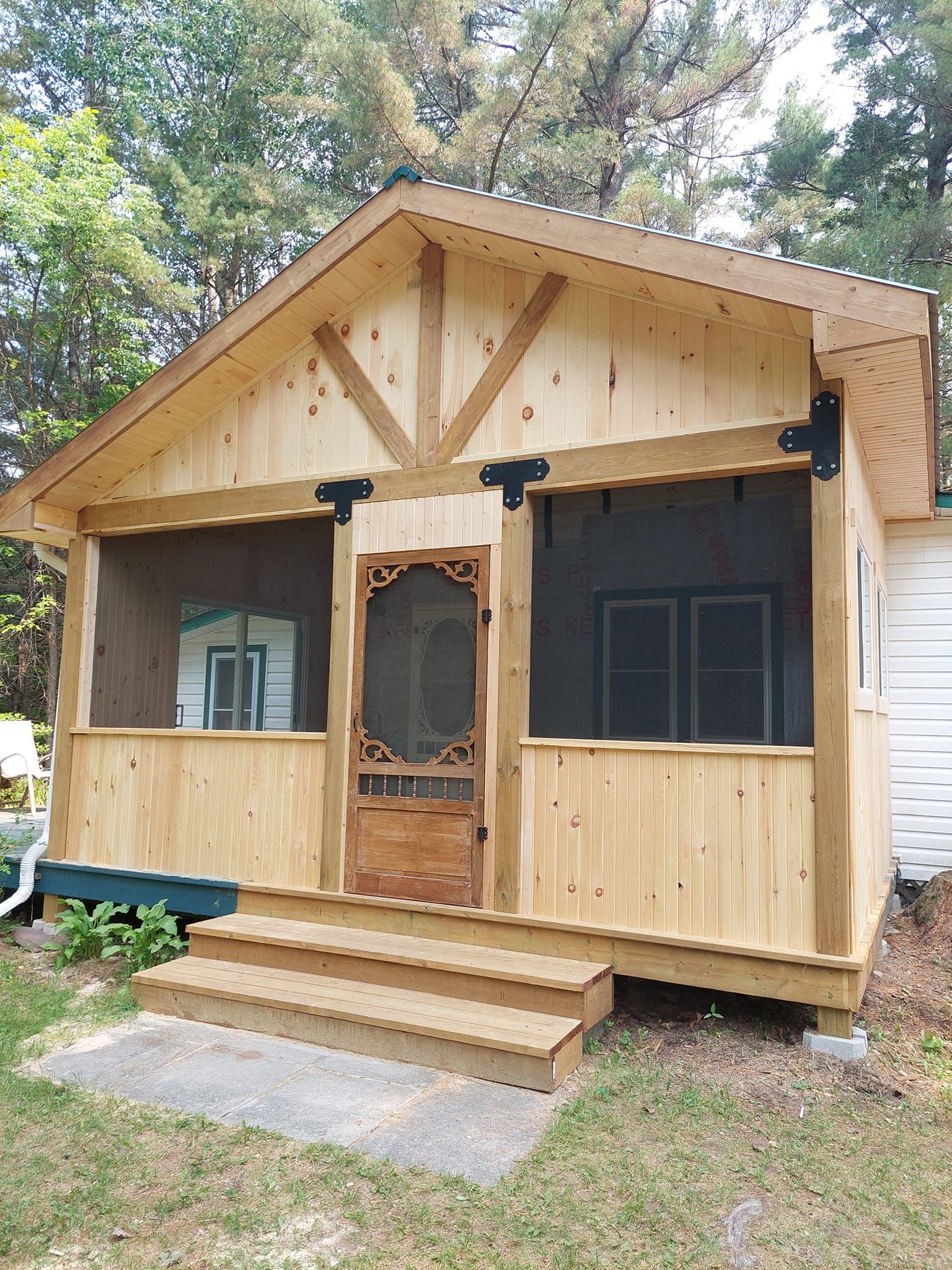 Wooden cabin with a screened porch and steps leading up to the entrance, surrounded by trees.