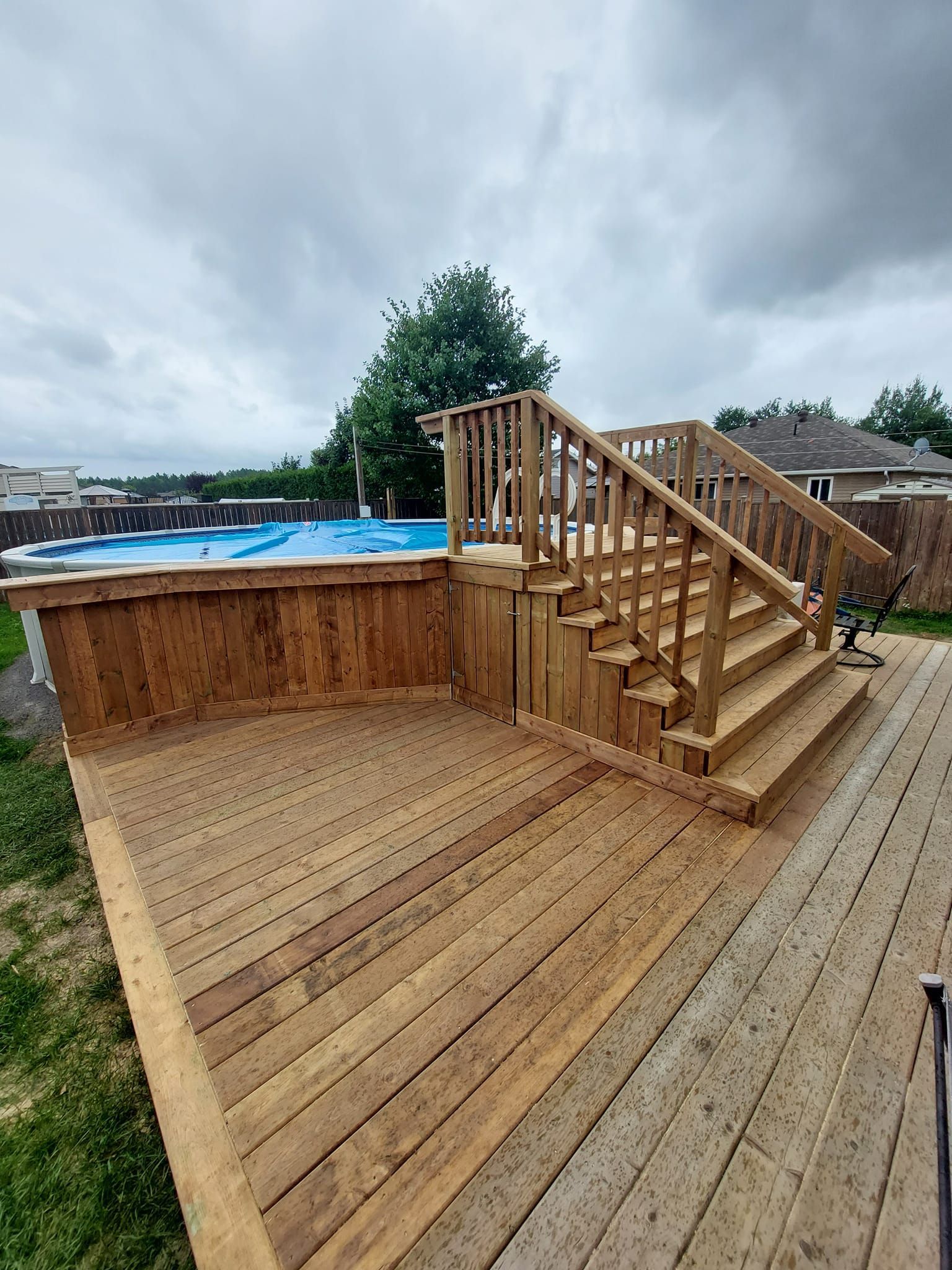 Wooden deck with stairs to a pool, overcast sky.