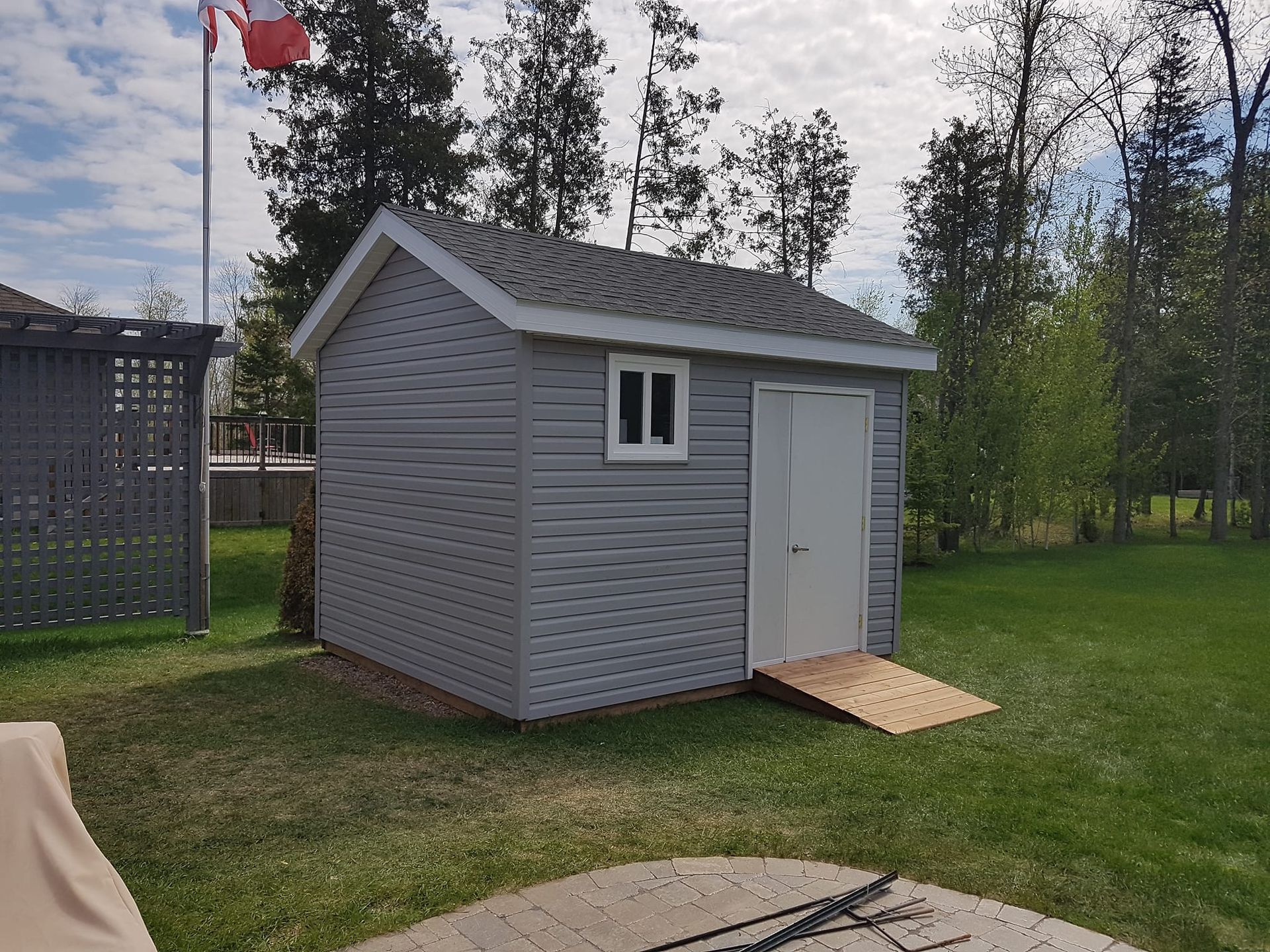 Gray shed with white door and window, wooden ramp, in a backyard.