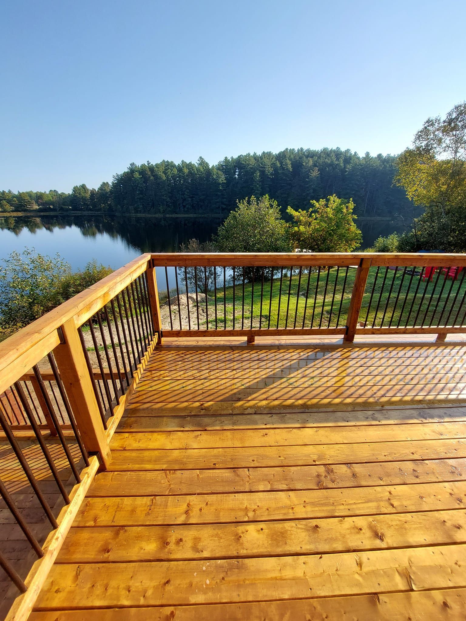 Wooden deck overlooking a calm lake and trees under a blue sky.