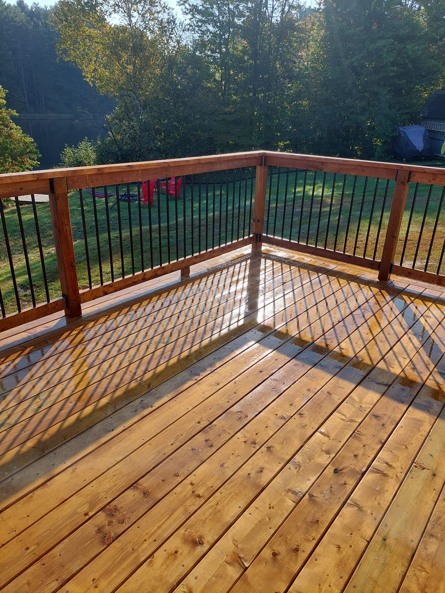 Wooden deck with dark metal railing, wet from recent rain, overlooking trees.