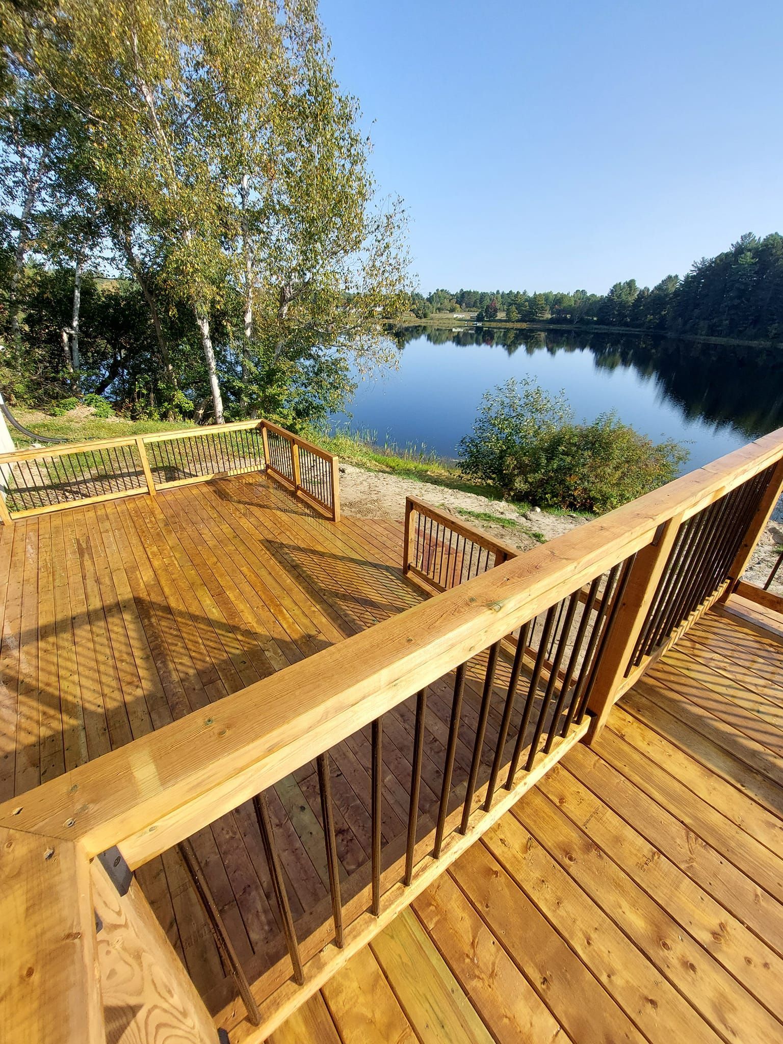 Wooden deck overlooking a calm lake, trees and blue sky in the background.