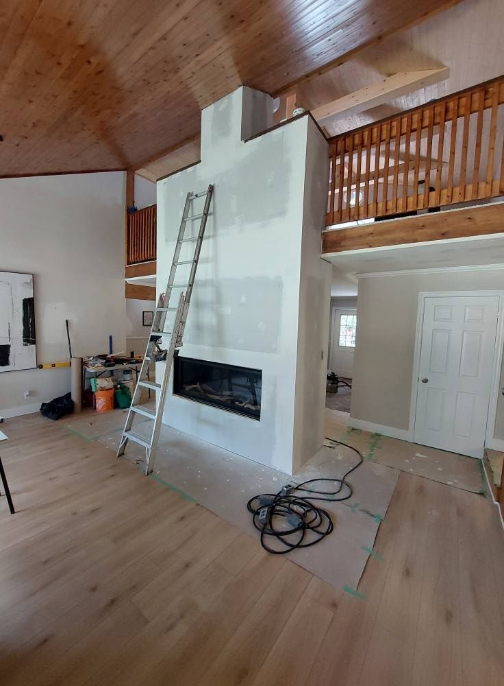 A room being renovated, with a fireplace and ladder, a loft area, and wood flooring.