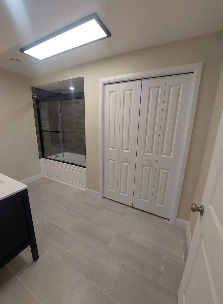 Bathroom with white bi-fold doors, gray tile, bathtub with glass door, and a dark vanity.
