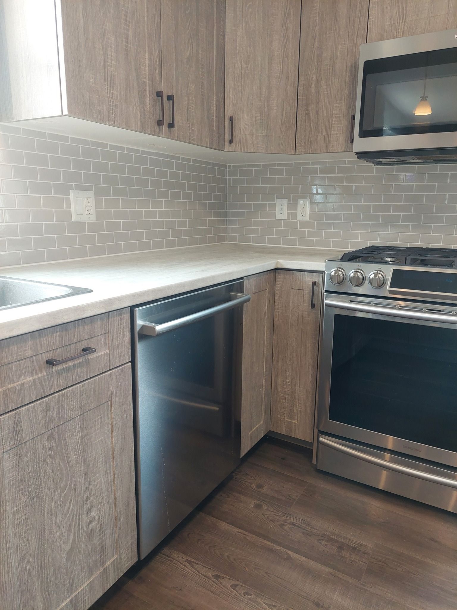 Modern kitchen with gray cabinets, stainless steel appliances, and white countertops.