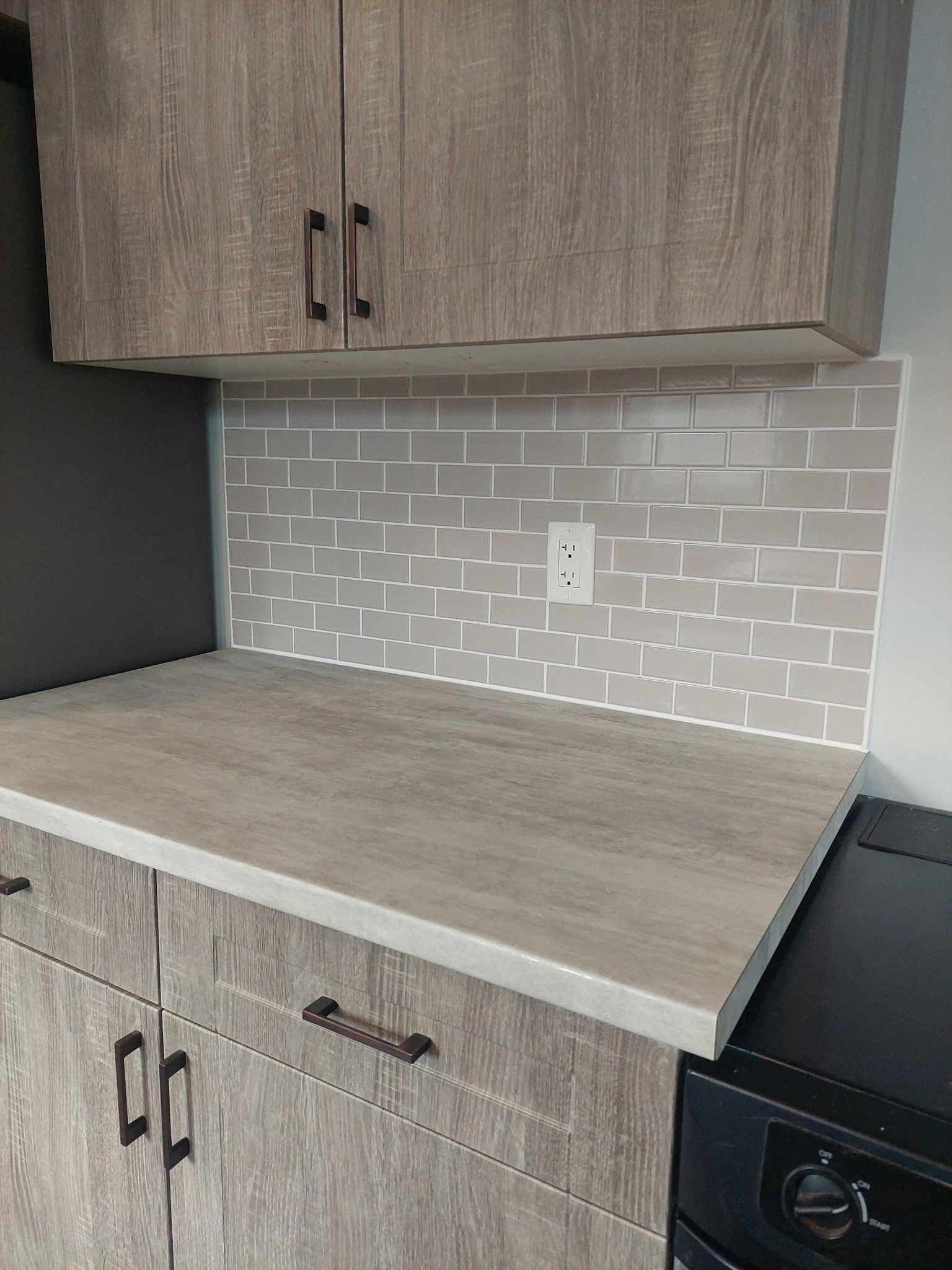 Gray cabinets with a matching countertop and brick-patterned backsplash, near a black appliance.