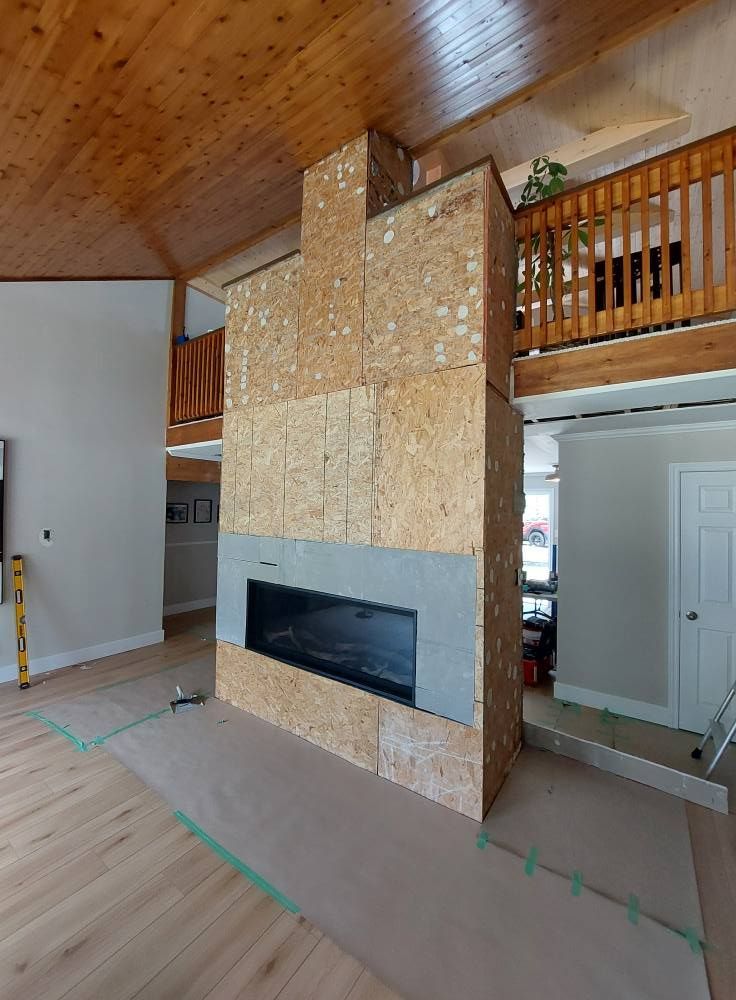 Fireplace under construction, OSB panels surround a modern fireplace with grey surround, light wood floor, and balcony.