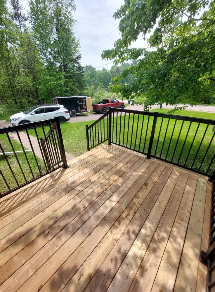 Wooden deck with black railings. Cars and trees in the background on a sunny day.