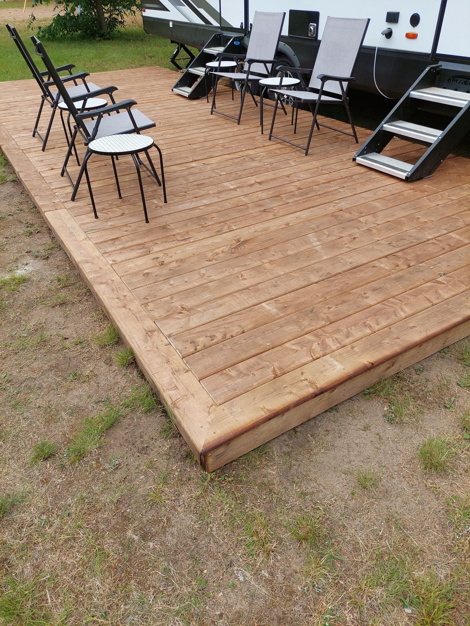Wooden deck with chairs beside a camper in an outdoor setting.