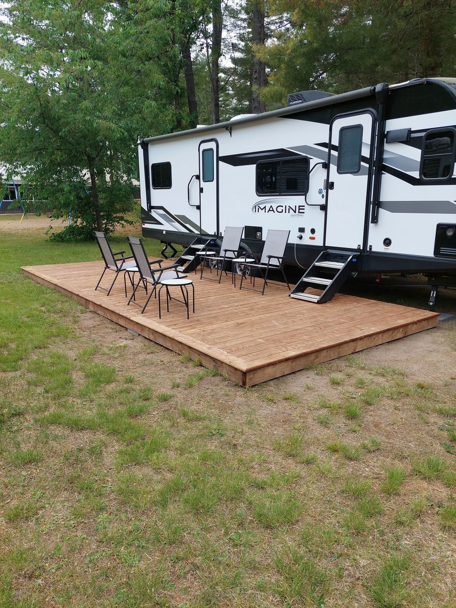 RV parked on a wooden platform with four chairs on a grassy campsite.