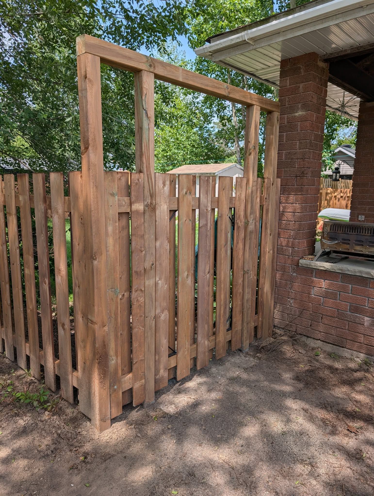 Wooden fence with a gate near a brick column of a building.