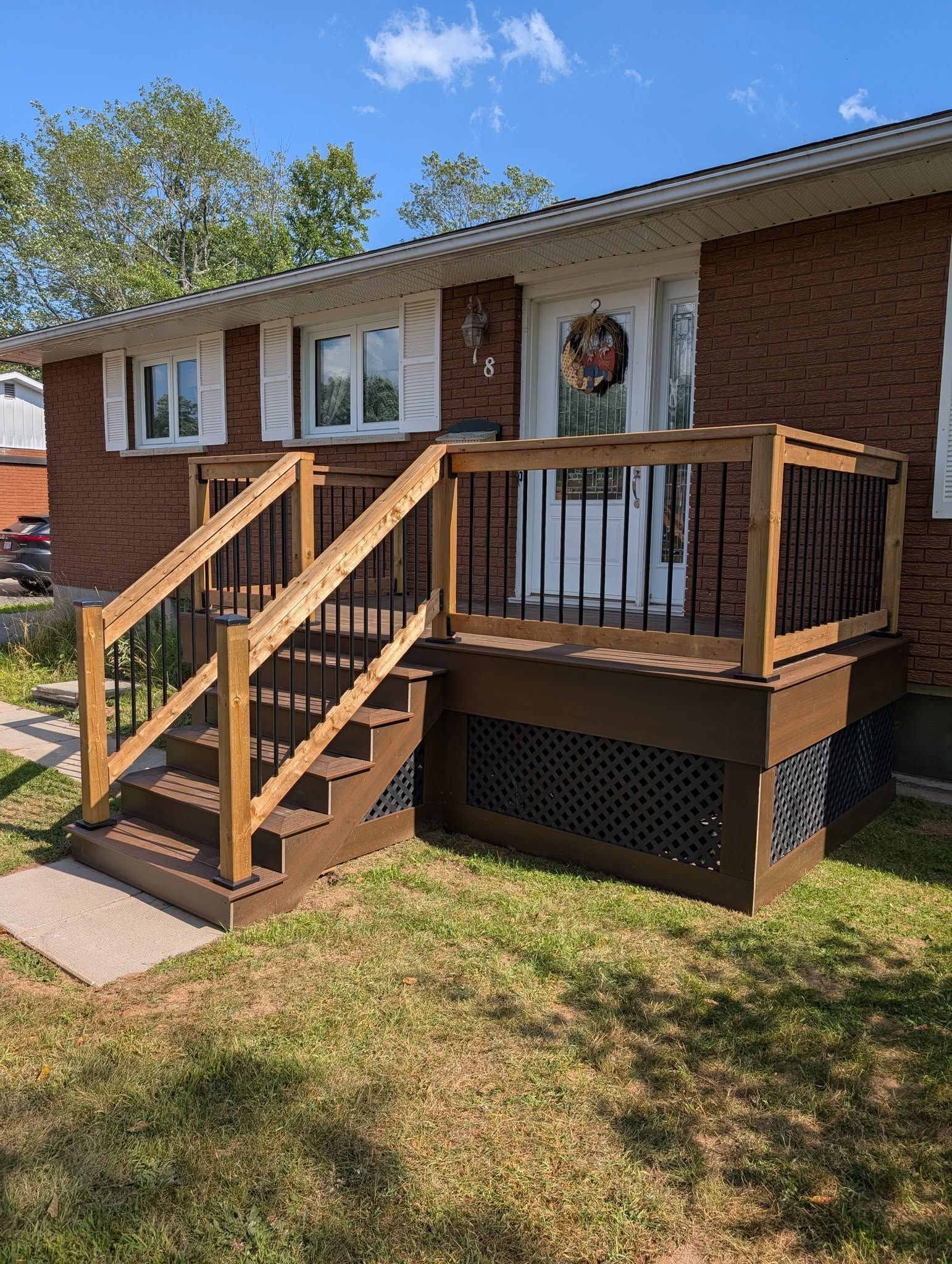 A brick house with a brown deck and stairs, surrounded by green grass.