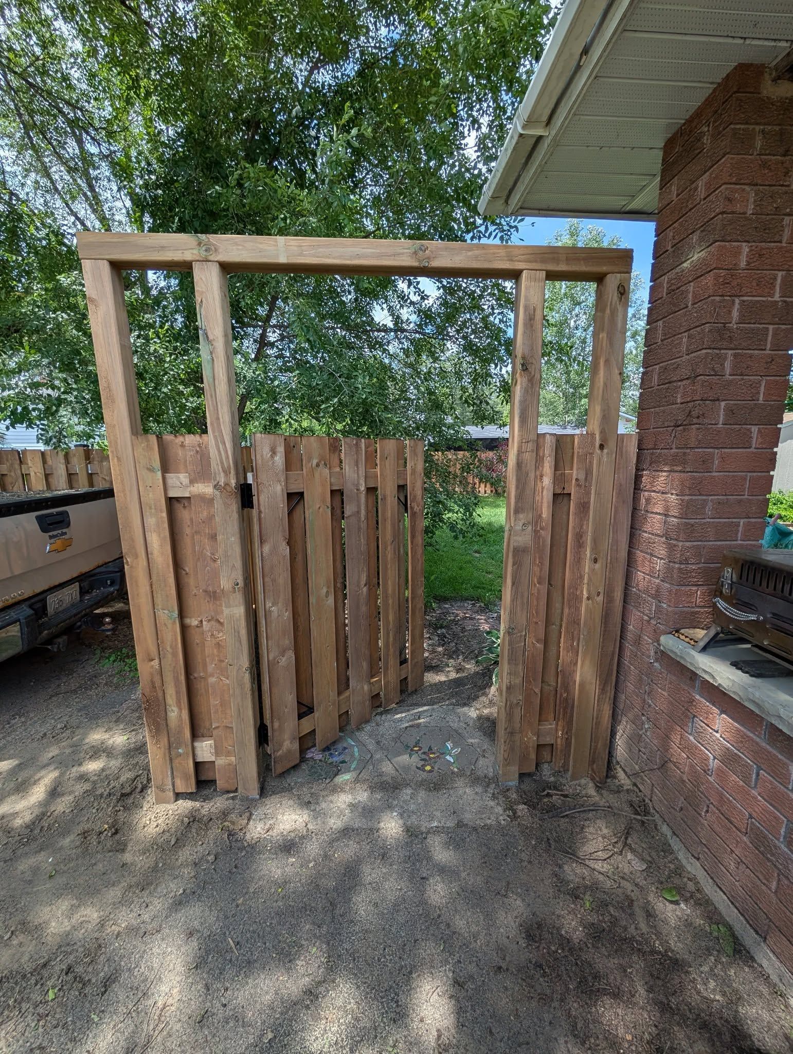 Wooden gate in a brick and dirt setting, leading to a grassy area.