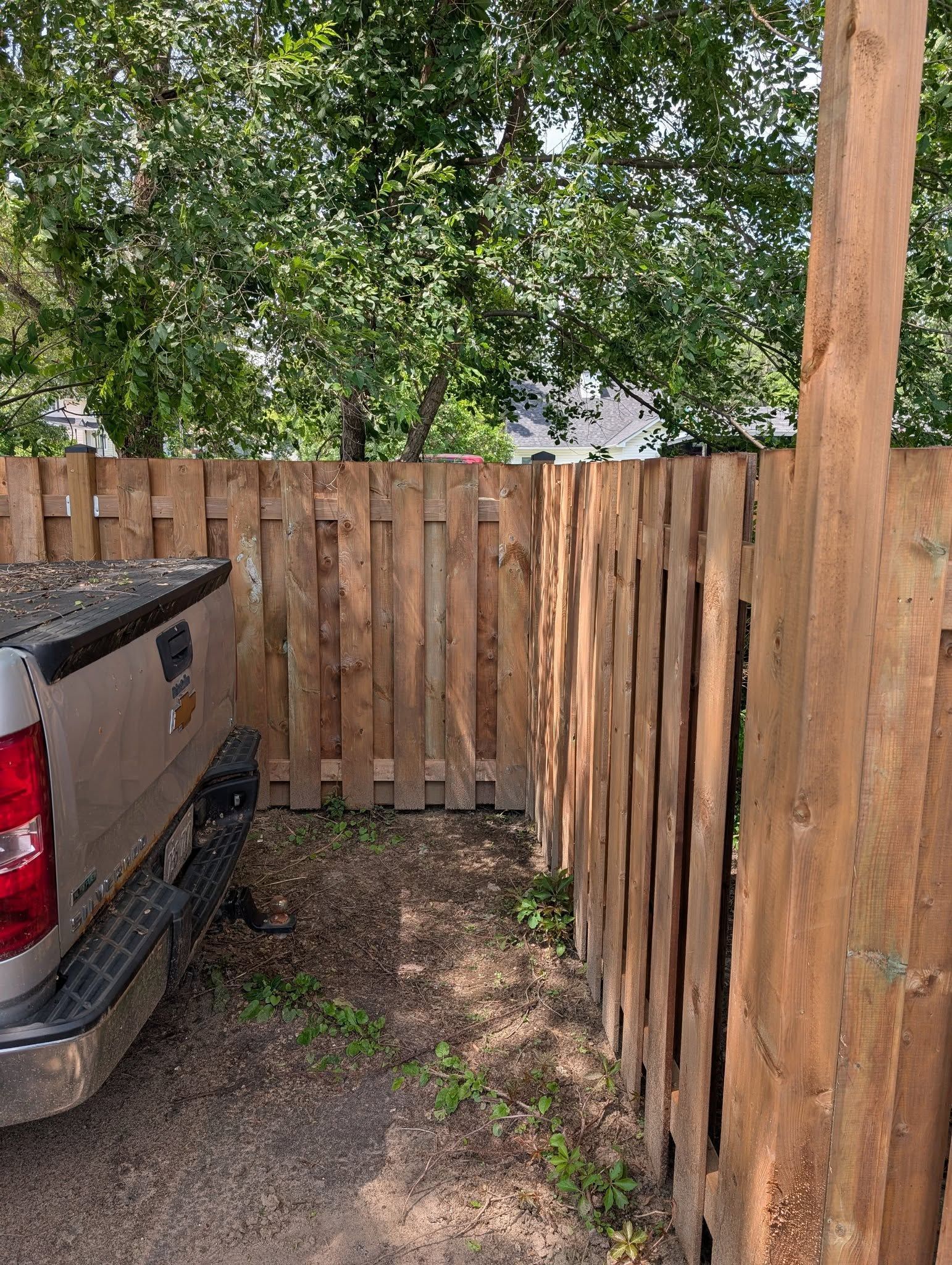 Truck parked next to a wooden fence, in front of a green tree.
