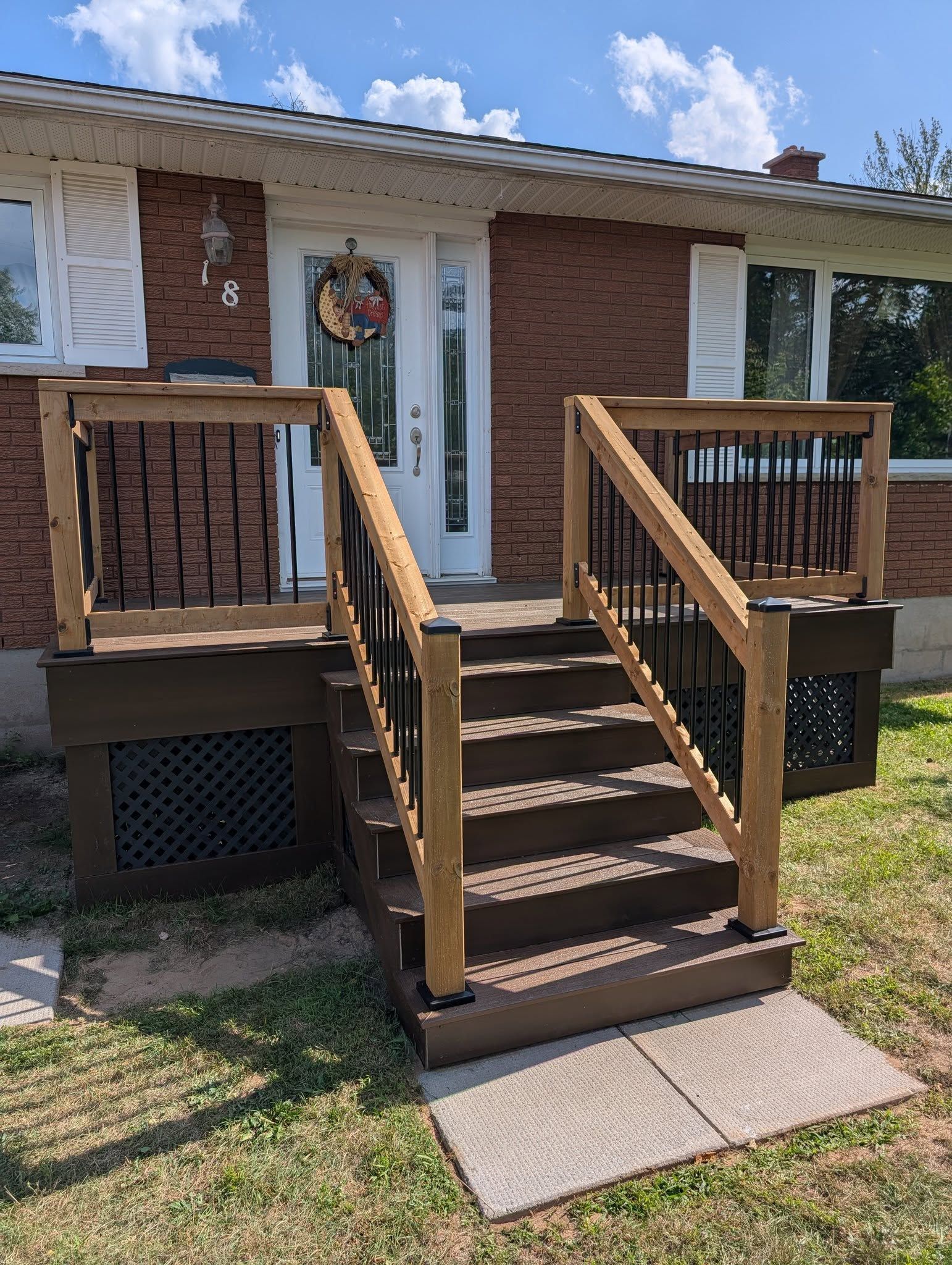 A brick house with a wooden deck and stairs leading to the front door, beige and brown colors.