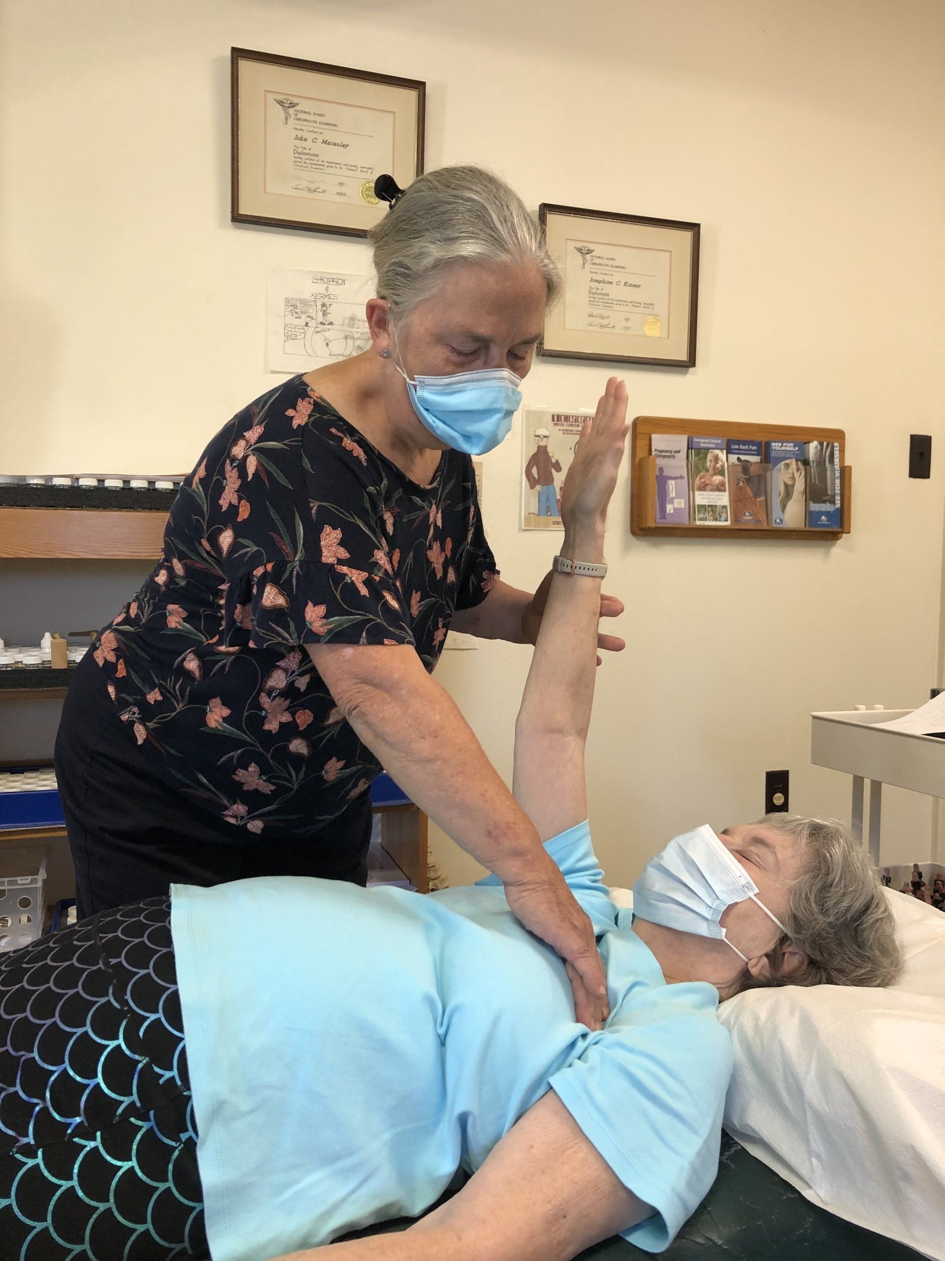 A woman wearing a mask is giving an older woman a massage.