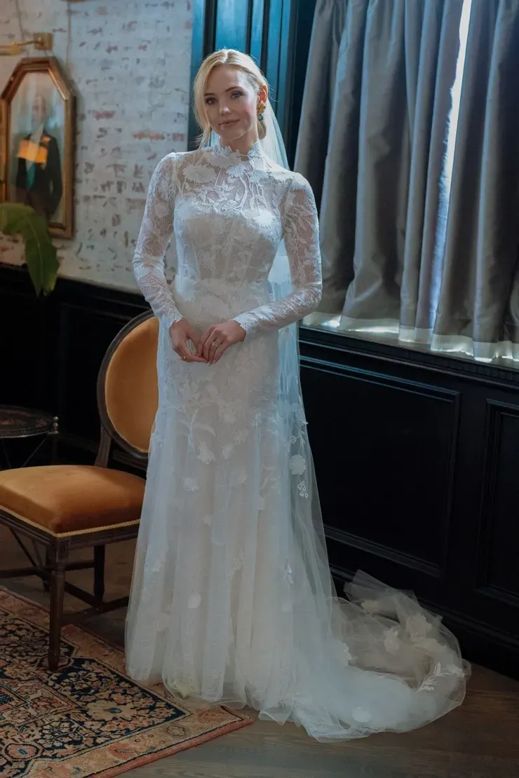 A woman in a wedding dress and veil is standing in front of a window.