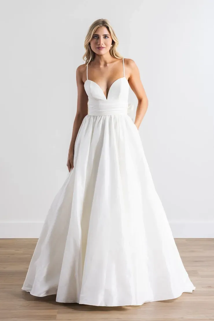 A woman in a white wedding dress is standing on a wooden floor.