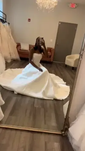 A woman is taking a picture of herself in a wedding dress in front of a mirror.