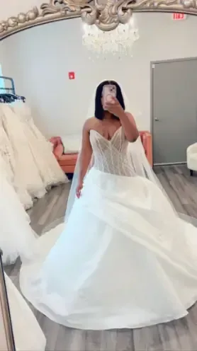 A woman in a wedding dress is taking a selfie in front of a mirror.