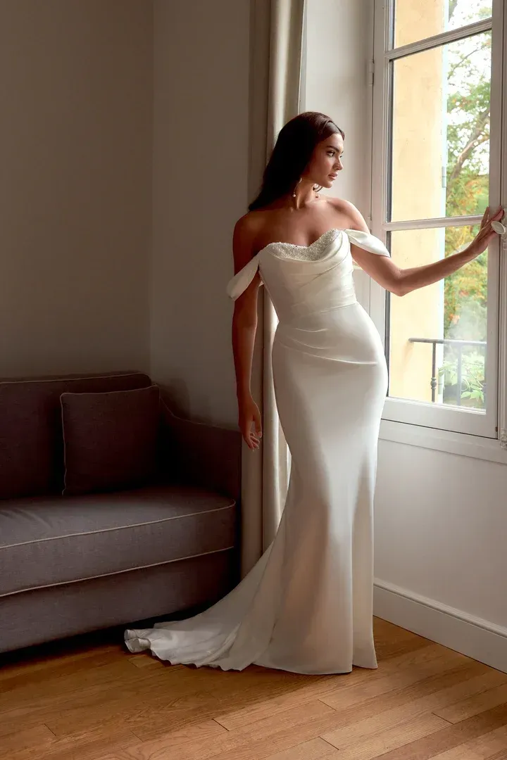 A woman in a white wedding dress is standing in front of a building.