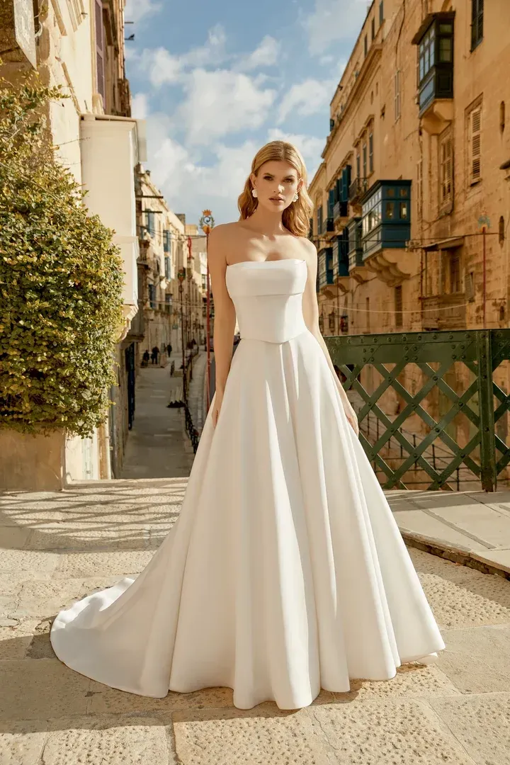 A woman in a white wedding dress is standing in front of a building.