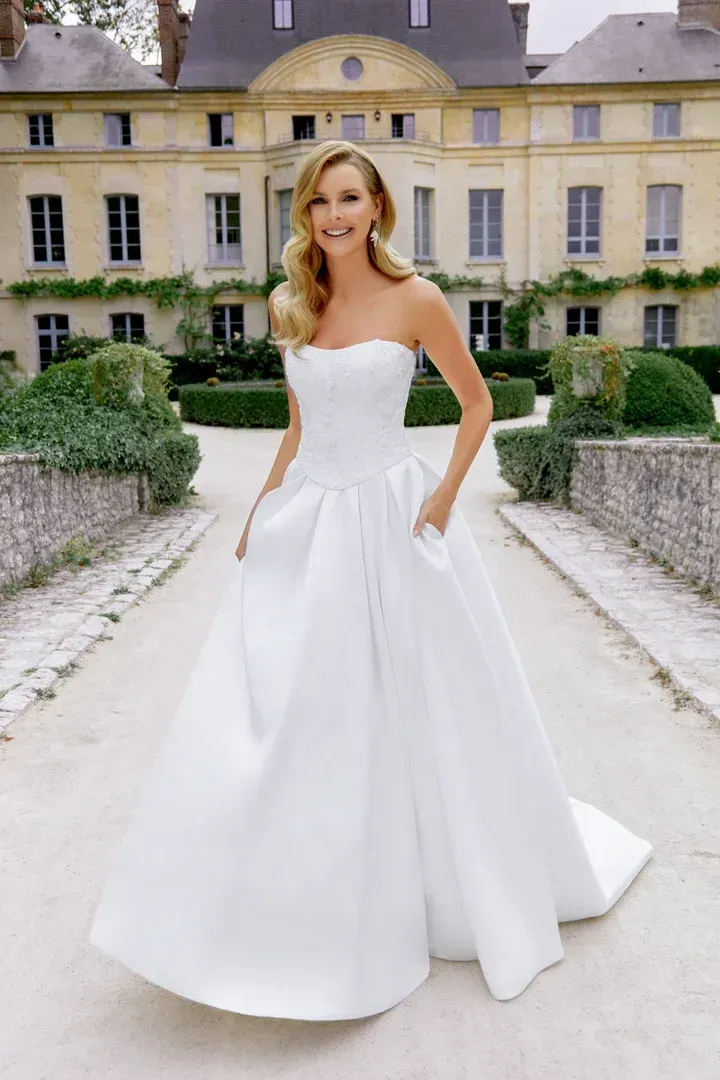 A woman in a white wedding dress is standing in front of a building.
